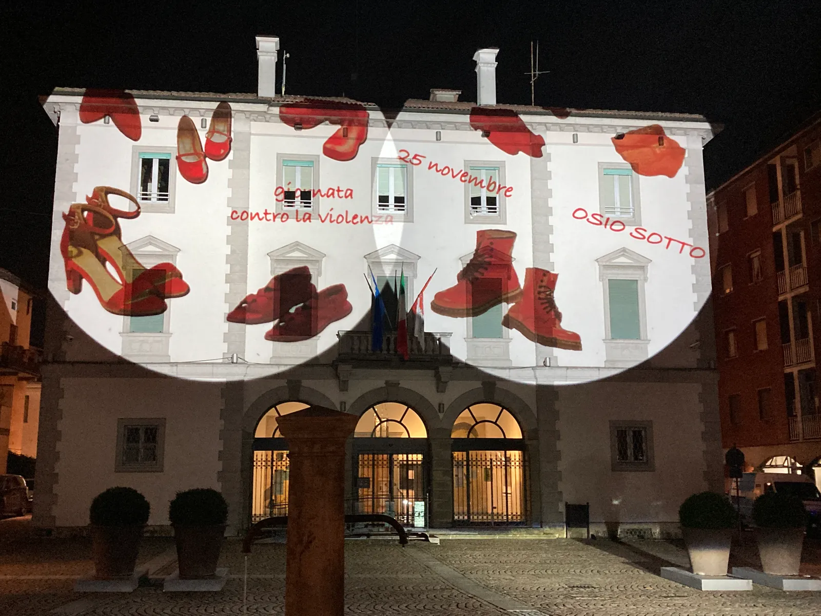 Facciata del municipio di Osio Sotto di notte, con scarpe rosse proiettate da due proiettori su tutto il piano alto: giornata contro la violenza sulle donne, 25 novembre 2021